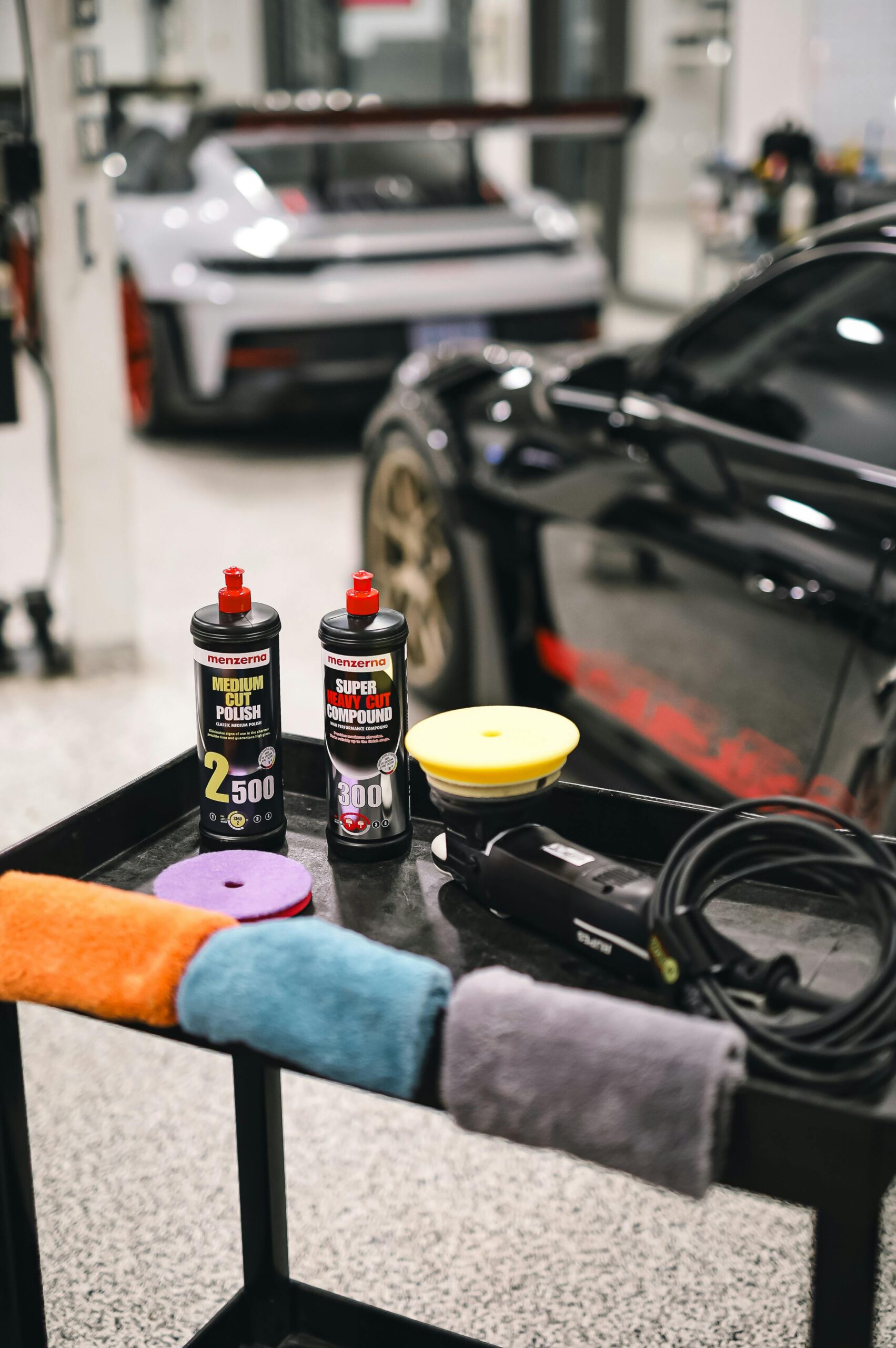 Car detailing products and equipment on table in modern garage with sports cars.