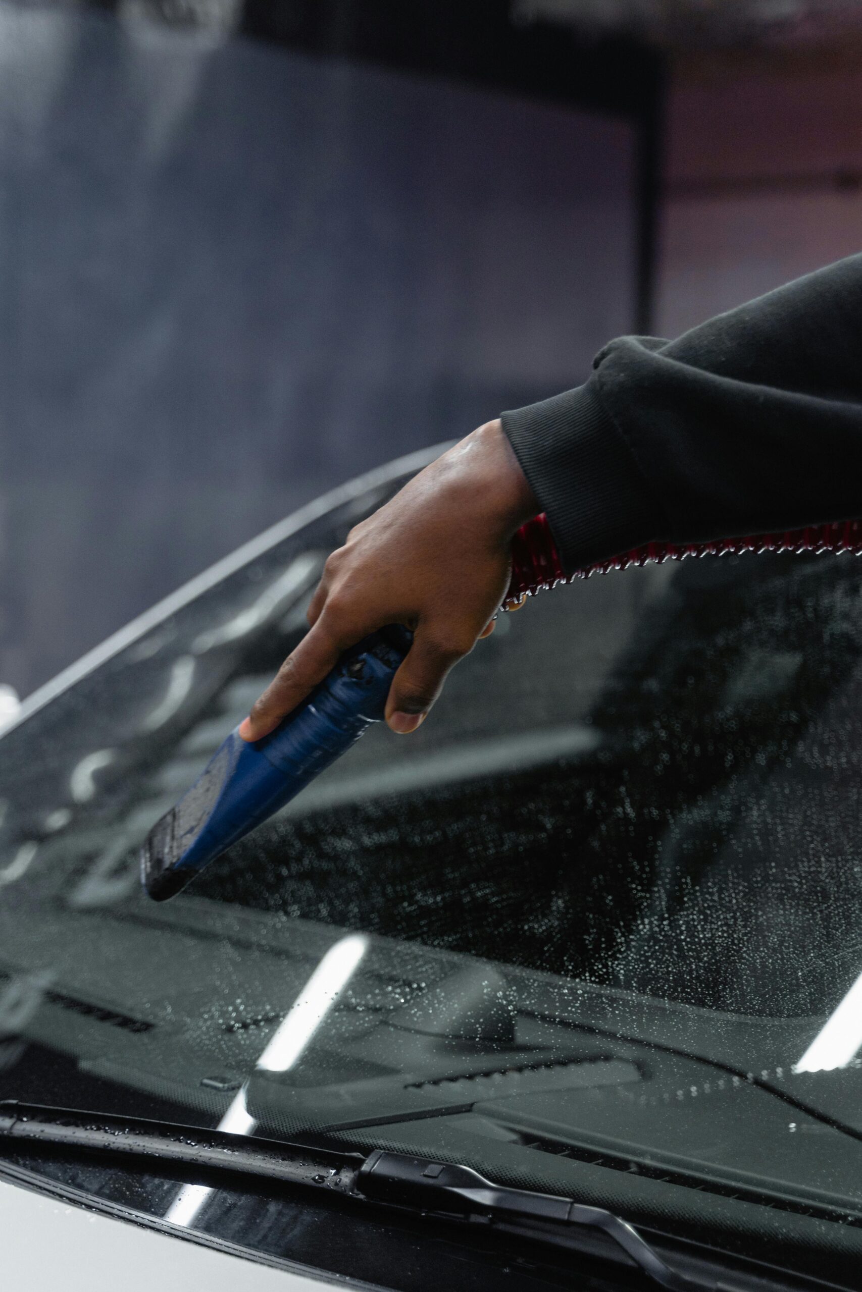 Close-up of a hand using a blower tool to dry a car windshield at an indoor carwash.